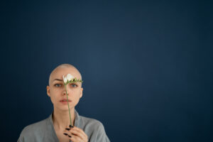 Woman with blossoming freesia and shaved head on blue background