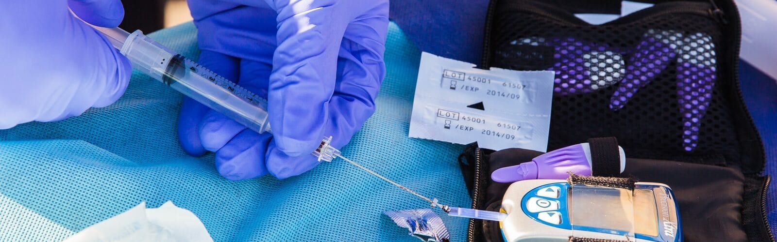 person using disposable syringe put specimen on blue and white glucose meter