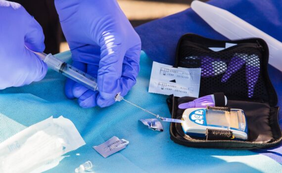 person using disposable syringe put specimen on blue and white glucose meter